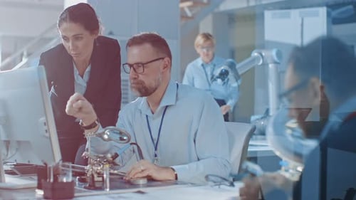 Chefingenieurin spricht mit einem Elektronikspezialisten, erklärt Dinge, er arbeitet am Computer und