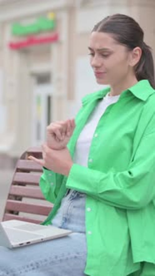 Woman Using Laptop On Bench Massages Her Wrist