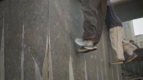 Young Men Climbing Over Urban Building Wall