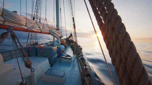 Sailing Vessel Moves in the Calm Glassy Open Sea with Sun Rising on the Horizon