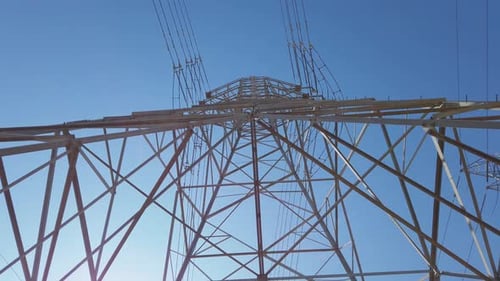 Electricity transformer tower on a blue sky backdrop with electric cable wires lines underneath look
