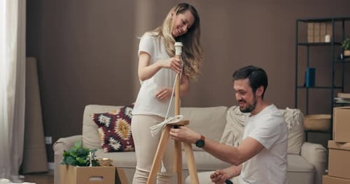 Moving in Process Delighted Husband Helping Adorable Young Wife Assembling New Floor Lamp in Modern