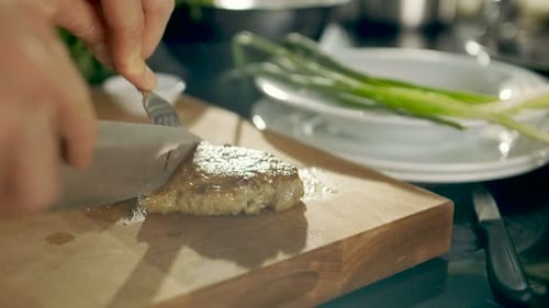 Close-up of Prepared Piece of Meat Being Cut with use of Knife and Fork on a Cutting Board. In Back
