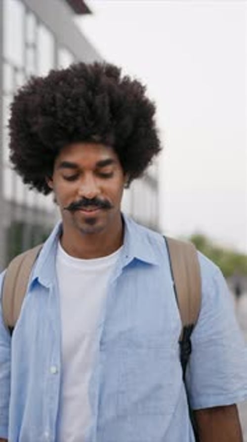 Joven afroamericano seguro de sí mismo caminando en la ciudad y sonriendo mirando a la cámara vertical