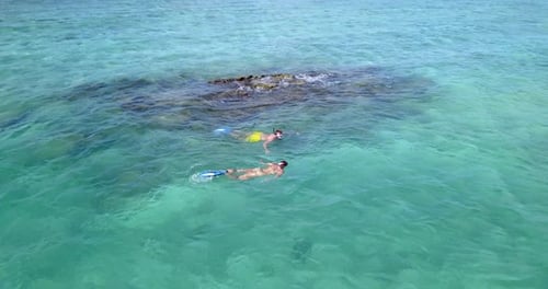 Aerial pan around young couple swimming together in crystal clear Maldives waters on beautiful sunny