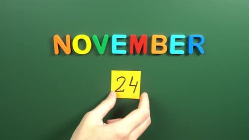 Hand sticking a sticker 24 November calendar day on school board. 24 date of November. Twenty fourh