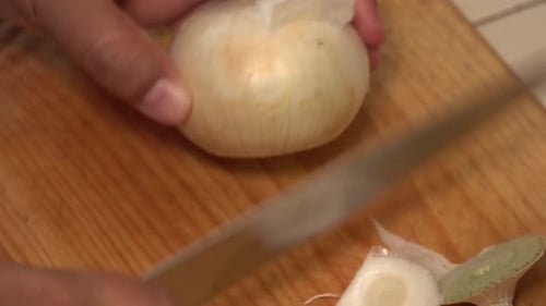 Person Peeling an Onion on Wooden Board