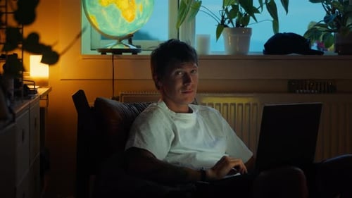 Junger erwachsener Mann arbeitet abends zu Hause am Laptop