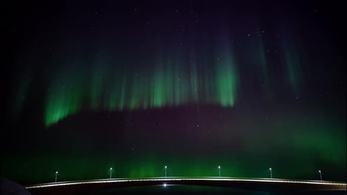 Dancing aurora borealis at night time over a illuminated bridge in Scandinavia. Handheld shot