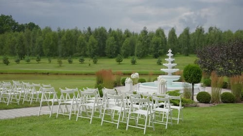 Outdoor wedding ceremony setup with white chairs and decorative fountain in a beautifully