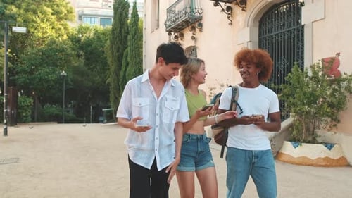 Multinational youth group walking with smartphones in the street on summer day