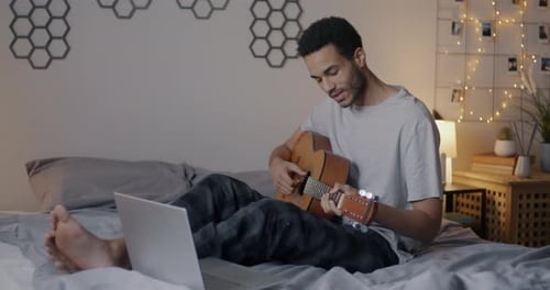 Young Adult Plays Guitar in Bedroom at Night