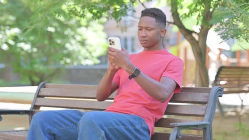Zufälliger afrikanischer Mann mit Smartphone im Freien im Park