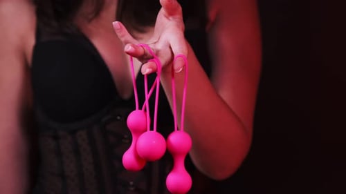 Woman's hand holds pink Kegel balls, Ben Wa balls on a black isolated background. Vaginal balls in a