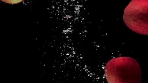 Drei rote Äpfel fallen in Zeitlupe in transparentes Wasser auf schwarzem Hintergrund