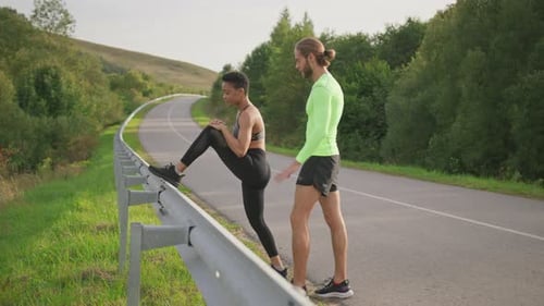 Afroamerikanische junge Läuferin streckt vor dem Training mit Unterstützung ihres Freundes die Beine