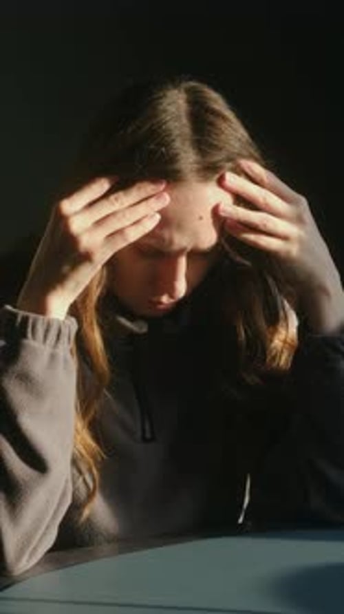 Young Woman Sitting in Dim Room Showing Signs of Distress and Inner Turmoil