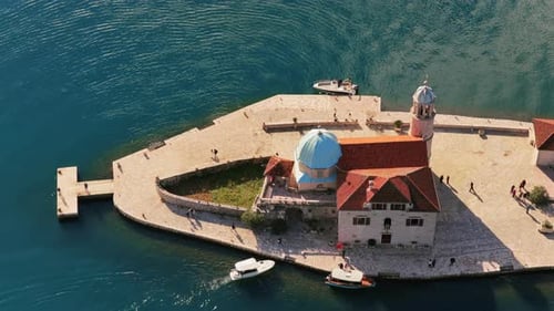 Aerial drone view of Saint George Island near Perast, featuring its stone monastery, cypress trees,