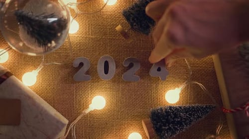 Rollo B: manos de mujer ponen números de 2024 en una mesa decorada, ¡feliz Navidad y próspero año nuevo!