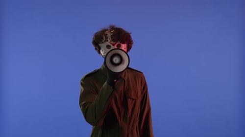 Man in White Mask with Loudspeaker in Hands on Blue Background with Red Neon Light Image of Maniac