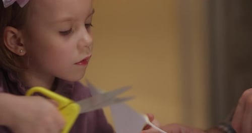 A Young Girl Carefully Cuts Paper Showing Focus and Joy in Her Creative Activity While Surrounded By