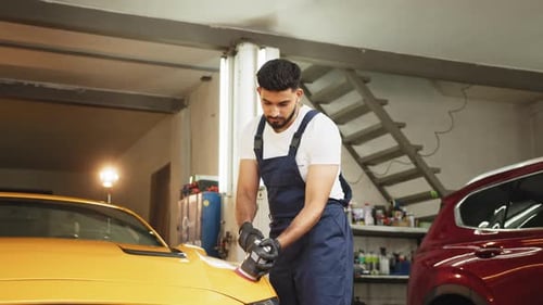 Man Polishing Yellow Car with Power Tool in Garage