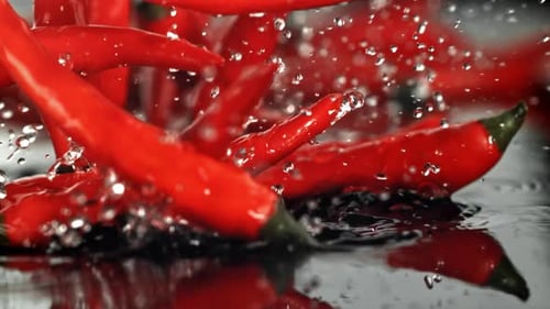 Chilischoten fallen auf eine nasse Oberfläche, gefilmt mit einer Hochgeschwindigkeitskamera mit 1000 Bildern pro Sekunde