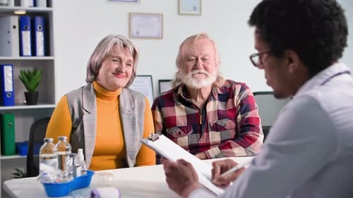 Health Care Elderly Couple at Reception of a Black Male Doctor in a Medical Office