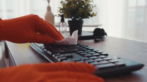 Hands in Gloves Cleaning Computer Keyboard with Wipe