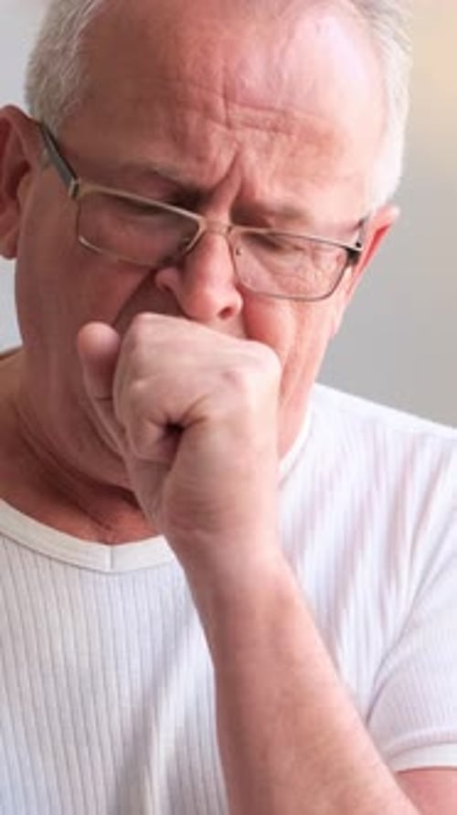 An Elderly Man Coughs in a Warm Setting Expressing Concern Distress and Vulnerability