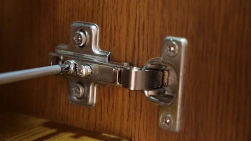 Tightening Hinge Screw on Wooden Cabinet Close Up