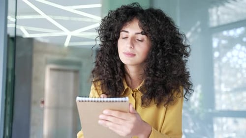 Webcam view. Young female employee watching video call training notes in a notebook looking at camer