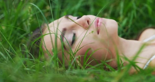 4k footage of an attractive young woman lying on a grass field by herself outside during the day