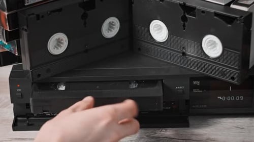 Hand inserts VHS tape into black VCR