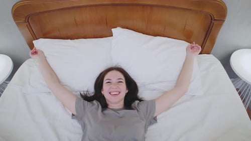 From a Topdown View a Brunette Woman Happily Falls Onto Her Bed The Scene Captures Comfort