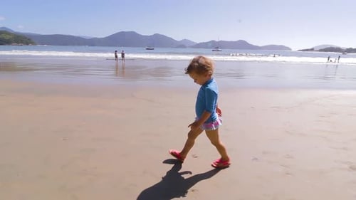 camera orbiting around young cute girl walking on the beach with mountains background and calm sea