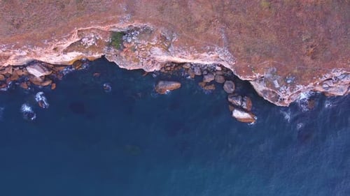 Top down aerial view of waves splash against rocky seashore, background. Flight over high cliffs of
