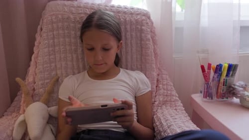 Girl Sitting in Chair Playing on Tablet