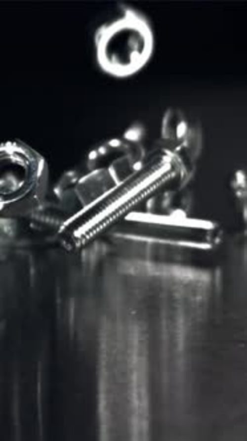 Varios tornillos, tuercas y arandelas caen sobre la superficie metálica, filmados con una cámara de alta velocidad a 1000 fps.