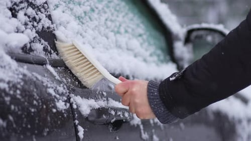 Cleaning Snow From Car Front Exterior Door with Brush During Snowfall Cyclone