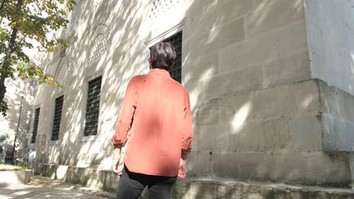 Back shot of Muslim young man walking by the fountain in a mosque garden , people visit historical
