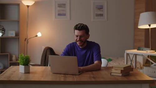A Young Man with Glasses Smiles and Types Something on a Laptop Young College Student Chatting with