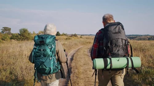 Senior Couple with Backpacks Hikes on Road at Autumn Countryside