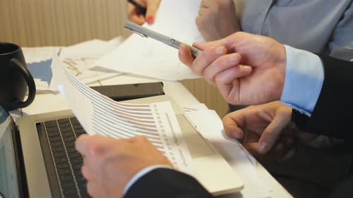 Nahaufnahme männlicher Hände des Chefs im Vergleich der Verkaufsergebnisgrafik auf Papier mit der Tabelle auf dem Laptop-Bildschirm unter