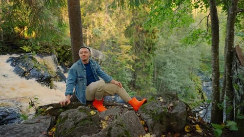 Tourist reist im Sommer im Reservat Park. Mann sitzt auf einem Stein am Flussufer im Wald