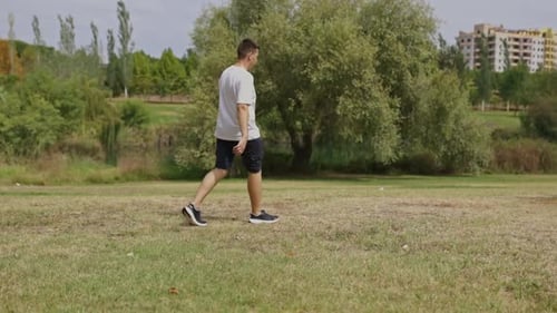 Young Man Walking on Grass in a City Park