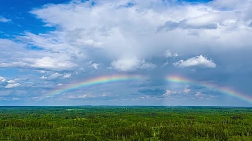 Arco-íris enquanto pancadas de chuva caem sobre um campo verde - paisagem nublada com lapso de tempo de drone