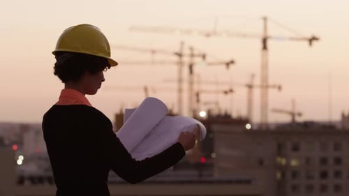 Architect Holding Plans Looking at Construction Site at Sunset Architect