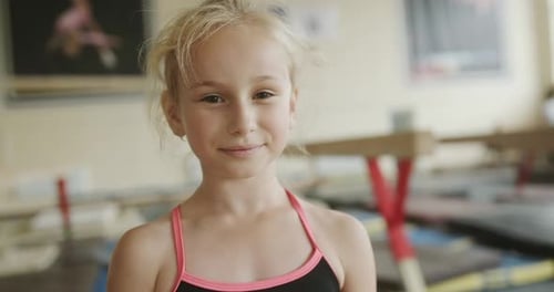 Little Gymnast During Training in Gym and Looking at Camera While Standing on Blurred Background of