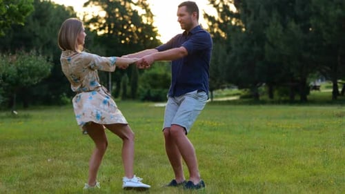 Cheerful Couple Having Fun in Green Park Holding Hands and Spinning Looking at Each Other Young